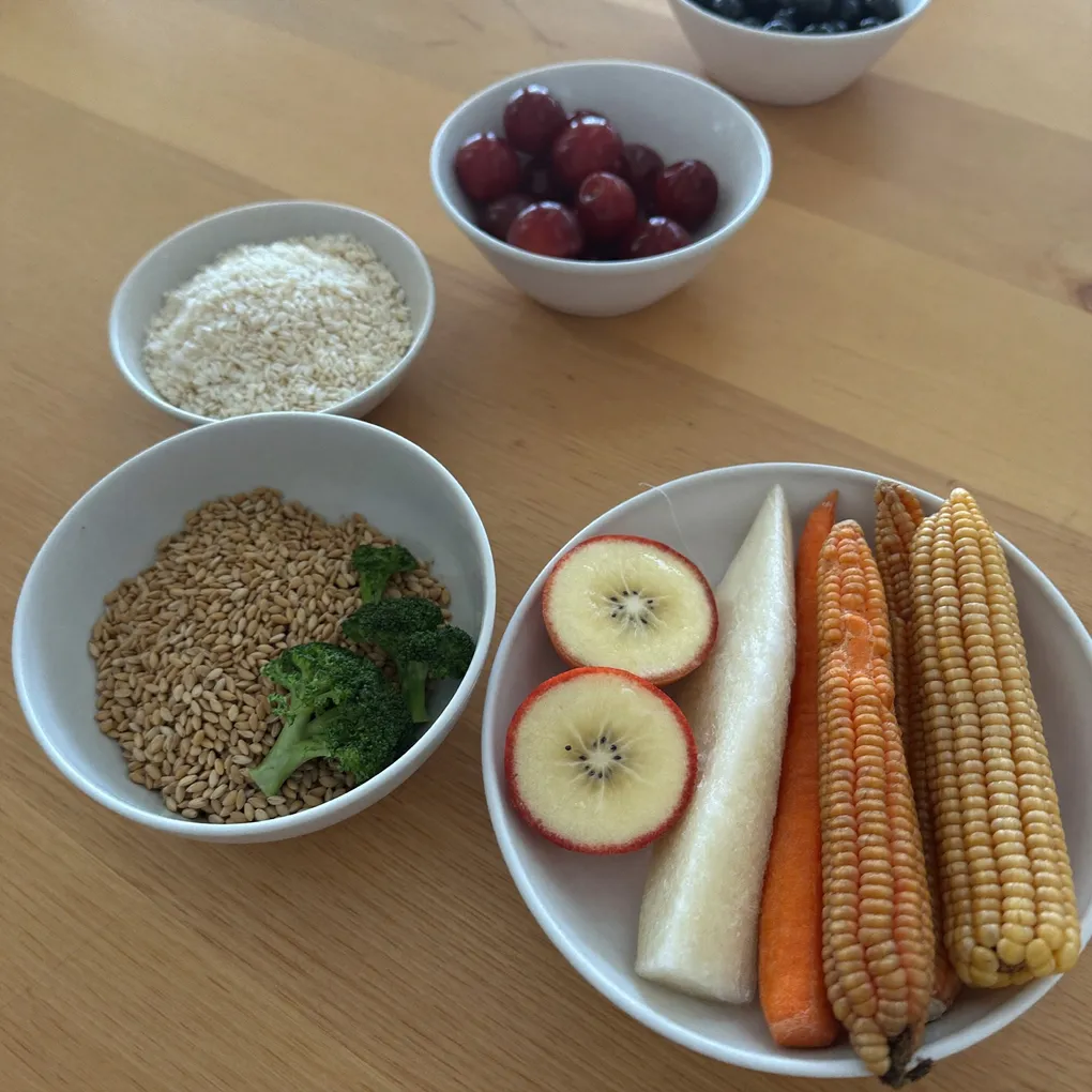 Schalen mit Getreide, Beeren, Apfel, Karotten und Mais auf einem Holztisch.