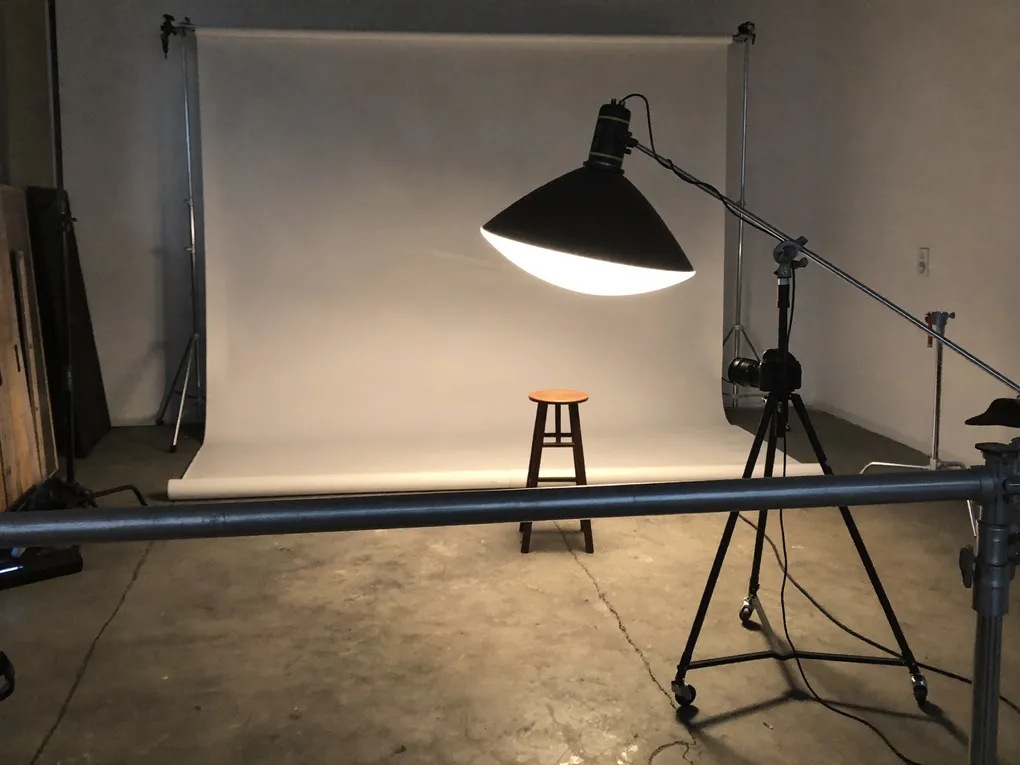 Leeres Fotostudio mit weißem Hintergrund, Hocker und einer Studioleuchte.