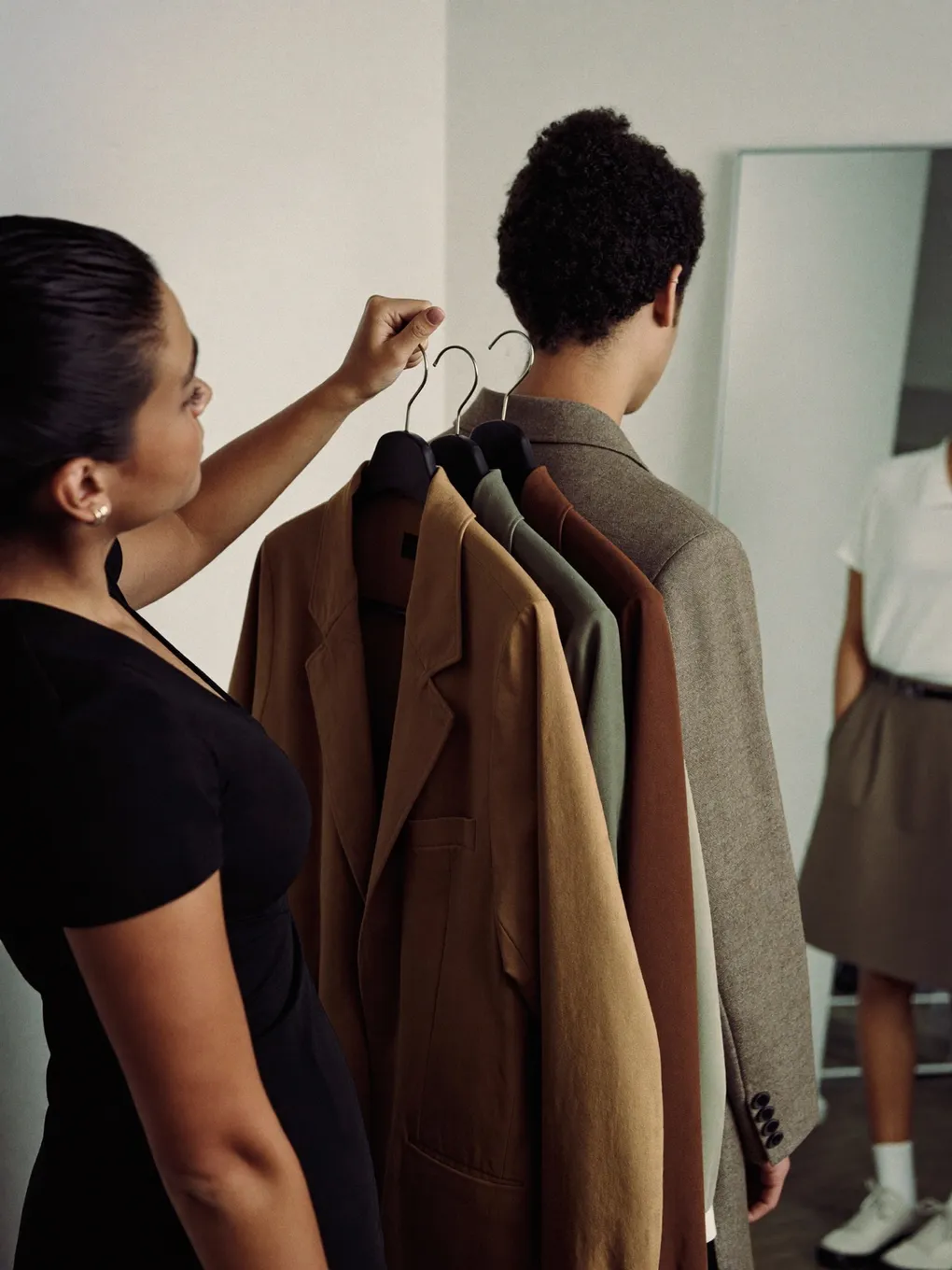 Stylistin sucht Mäntel von einer Kleiderstange aus, daneben ein Model.