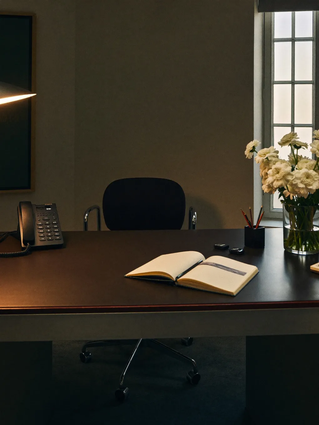 Aufgeräumter Bürotisch mit Telefon, offenem Notizbuch und Blumen.
