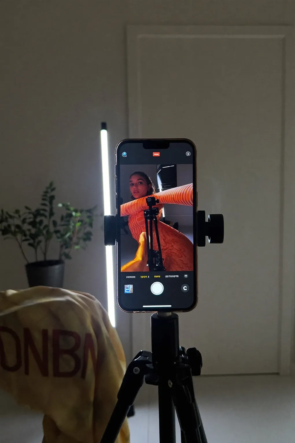 Smartphone mit LED-Leuchte auf Stativ, im Vordergrund ein gelbes Kleidungsstück.